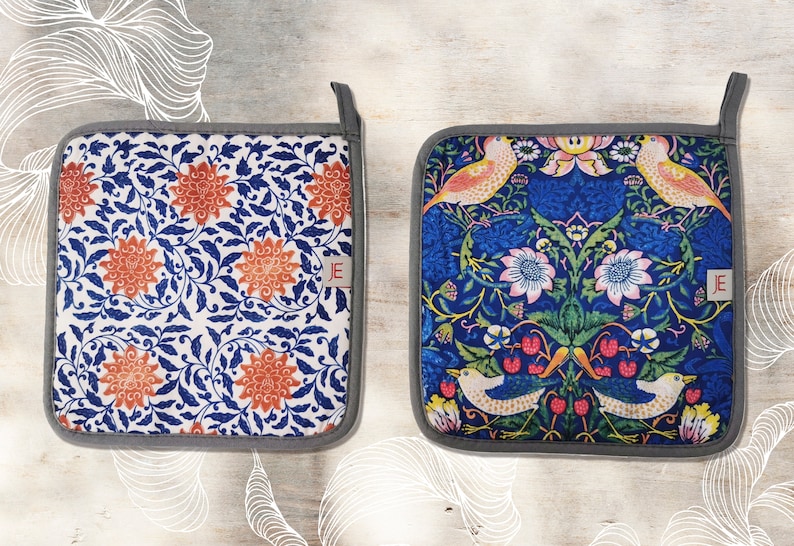 May include: Two square pot holders with a gray border. One pot holder has a white background with a blue and orange floral pattern. The other pot holder has a blue background with a floral pattern featuring birds and berries. Both pot holders have a small white tag with the letter "E" in red.