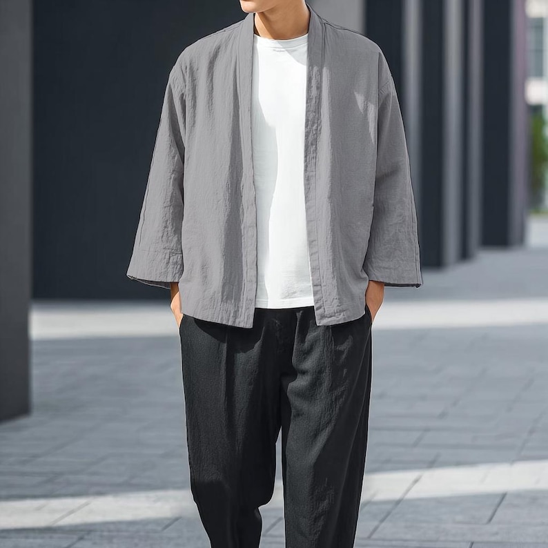 May include: A grey, open-front kimono-style jacket with three-quarter sleeves. The jacket is worn over a white t-shirt and paired with black trousers. The outfit is casual and appears to be made of a lightweight fabric.