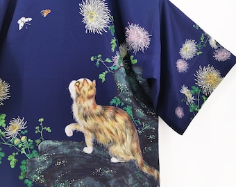 May include: A navy blue kimono featuring a cat, butterflies, and white flowers printed on it.