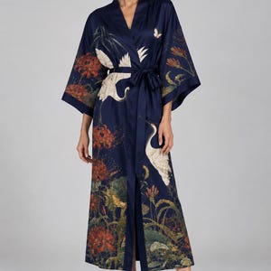 May include: A floor-length navy blue robe with a wrap-front design and a tie waist. The fabric features a detailed print of white cranes, red spider lilies, and green foliage. The garment has wide, three-quarter length sleeves and a V-neckline.