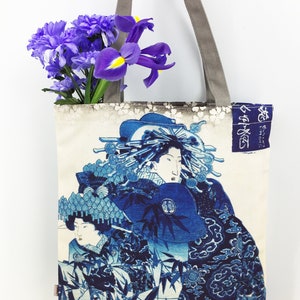May include: A blue and white tote bag with a Japanese print of two women in traditional clothing. The bag has a grey canvas strap and the text "御誂" is printed on the side.