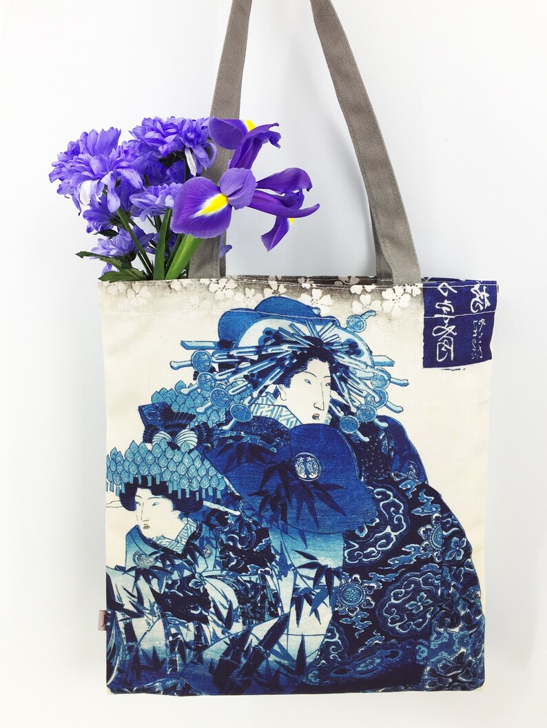 May include: A blue and white tote bag with a Japanese print of two women in traditional clothing. The bag has a grey canvas strap and the text "御誂" is printed on the side.