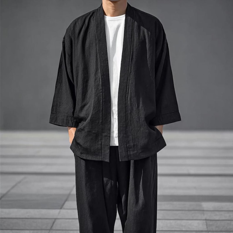 May include: A black kimono-style jacket with three-quarter sleeves and matching loose-fitting trousers. The jacket is open at the front, showing a white t-shirt beneath. The outfit is made of a lightweight fabric, suitable for casual wear.