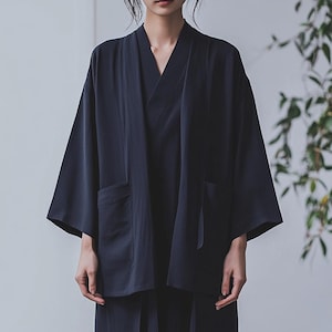 May include: A dark blue kimono-style jacket with long sleeves and a wide collar. The jacket has two pockets on the front and a tie belt at the waist.