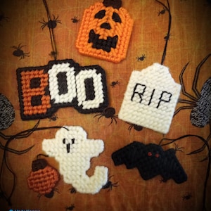 May include: A set of five Halloween-themed felt ornaments. The ornaments are shaped like a pumpkin, a ghost, a bat, a tombstone with the word "RIP" on it, and a sign that says "BOO". The ornaments are all white, black, and orange.
