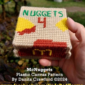 Può includere: Un modello di tela in plastica per una scatola di McNuggets. Il modello è nei colori rosso, giallo e verde. La scatola dice "McNuggets" e "4" sul davanti. Il modello è di Danita Crawford.