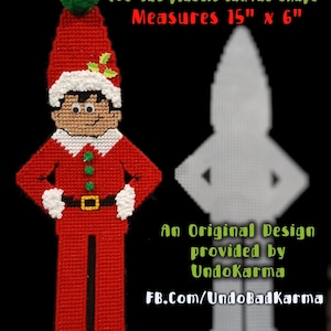 May include: A Flat Elf pre-cut plastic canvas shape measuring 15 inches by 6 inches. The elf is stitched in red, white, and green with a pom-pom hat, belt, and holly detail. Next to it is a plain white plastic canvas outline of the same elf shape.