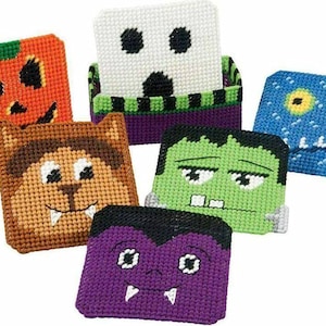 May include: A collection of six square, handmade coasters with Halloween-themed designs. The coasters feature a pumpkin, ghost, werewolf, Frankenstein's monster, vampire, and a blue monster. Each coaster is made with a cross-stitch technique.