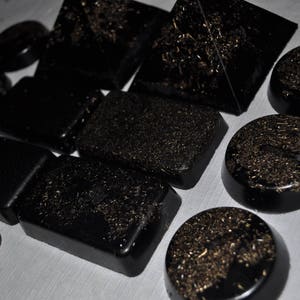 May include: A collection of black, gold-flecked, pyramid-shaped stones. The stones are arranged in a variety of sizes and shapes.