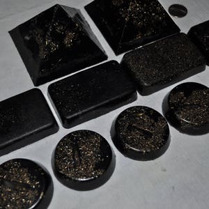 May include: A set of ten black pyramid-shaped resin coasters with gold glitter embedded in the resin. The coasters are arranged in a staggered pattern on a white surface.