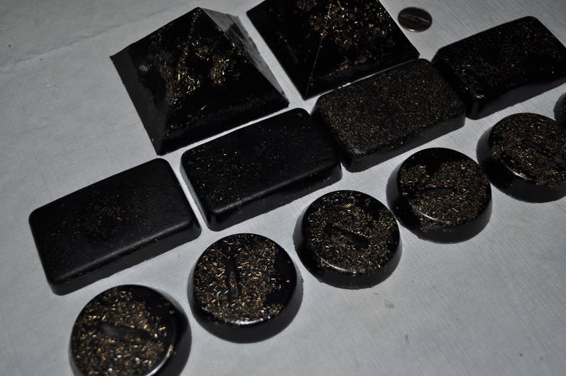 May include: A set of ten black pyramid-shaped resin coasters with gold glitter embedded in the resin. The coasters are arranged in a staggered pattern on a white surface.