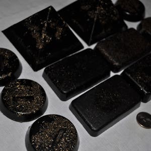 May include: A collection of black and gold coasters with a variety of geometric shapes and designs. The coasters are made of a smooth, polished material and have a subtle shimmer.