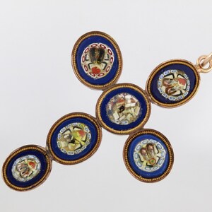 May include: A cross-shaped pendant composed of five oval micro-mosaic elements set in gold-toned metal. Each oval features a deep blue background with intricate, multi-coloured floral and geometric glass tile patterns and a small top bail.