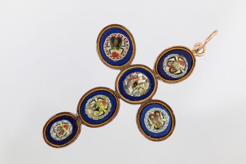 May include: A cross-shaped pendant composed of five oval micro-mosaic elements set in gold-toned metal. Each oval features a deep blue background with intricate, multi-coloured floral and geometric glass tile patterns and a small top bail.