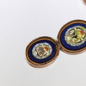 May include: A bracelet composed of oval links featuring deep blue enamel borders and central micro-mosaic floral patterns. Each link is framed in a metallic setting with a beaded edge, connected by small metal rings in a repeating sequence.