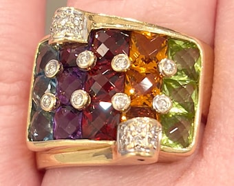 May include: A gold ring featuring a rectangular face with a mosaic of colorful gemstones. The gemstones include blue, purple, red, orange, and green stones, accented with small diamonds. The ring has diamond accents on the shoulders.