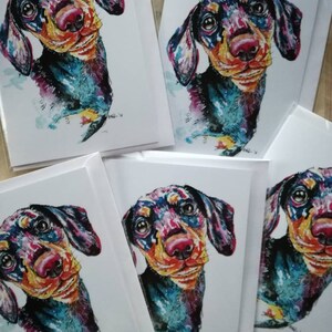 Op de afbeelding: Vijf blanco wenskaarten met kleurrijke aquarel illustraties van een teckel. De hond kijkt recht naar de kijker met een speelse uitdrukking. De kaarten zijn perfect om een speciale boodschap naar een geliefde te sturen.
