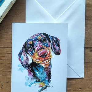 Op de afbeelding: Een kleurrijk aquarel schilderij van een teckel met grote ogen en een speelse uitdrukking. De hond is geschilderd in tinten blauw, roze, geel en zwart.
