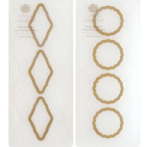 May include: Two sheets of clear silicone with gold-colored shapes. The left sheet has four diamond-shaped stencils. The right sheet has four oval-shaped stencils. The text on the sheets reads "Anna Griffin Oblong Silicone Cut & Emboss Folder Made in China" and "Anna Griffin Suzani Silicone Cut & Emboss Folder Made in China".