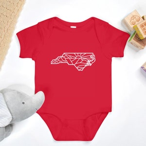May include: Red baby onesie with a white outline of the state of North Carolina, featuring mountains and a sunrise.