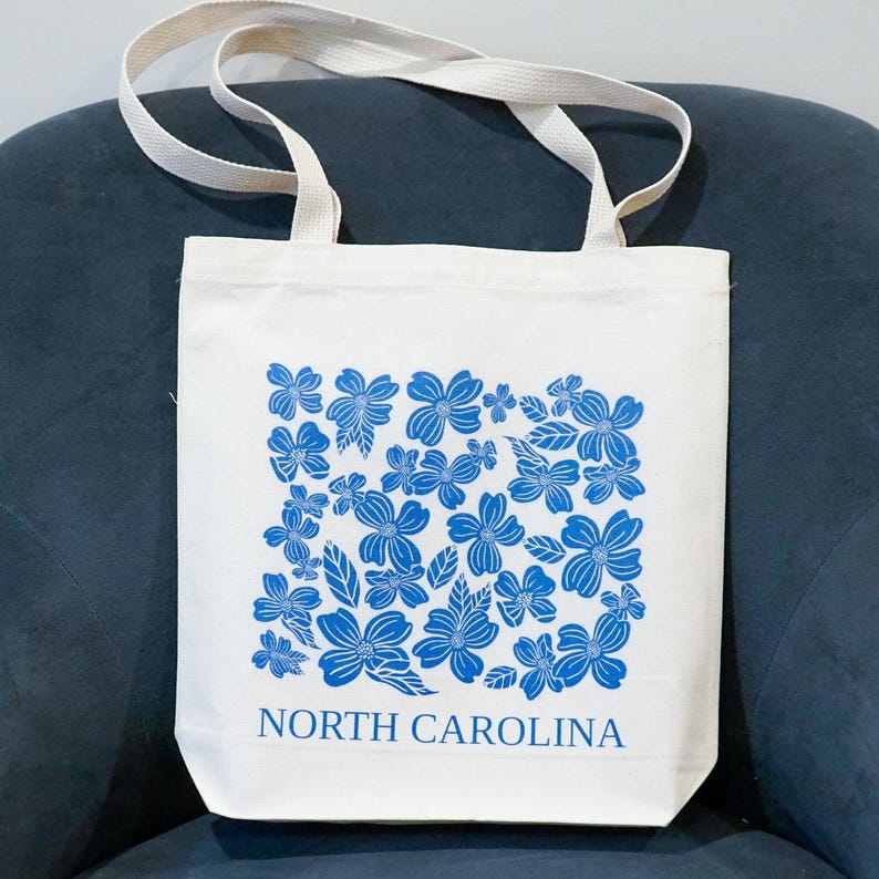 May include: A white canvas tote bag with blue floral print and the text "NORTH CAROLINA".