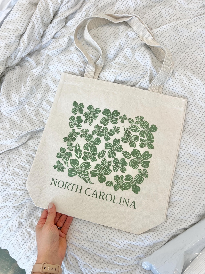 May include: A beige canvas tote bag with green floral print and the text "NORTH CAROLINA".