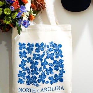 May include: A white canvas tote bag with blue floral print and the text "NORTH CAROLINA".