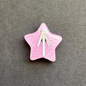 May include: A pink glitter star with a silver arrow pointing upwards.