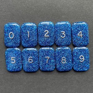 May include: Ten blue, glittery, square tiles with white numbers 0 through 9.