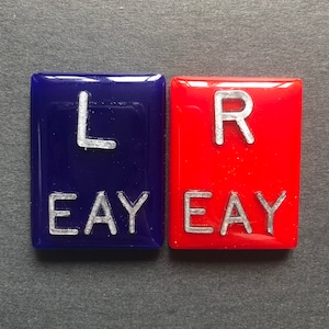 May include: Two square tiles, one blue and one red, with the letters "L" and "R" in silver lettering. The word "EAY" is printed below each letter.
