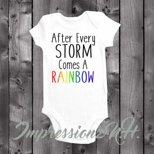 May include: White baby onesie with the text "After Every STORM Comes A RAINBOW" in black. The word "RAINBOW" is in rainbow colors.
