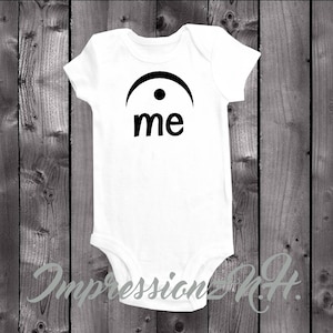 May include: White baby onesie with a black musical note symbol and the word "me" printed on the front.