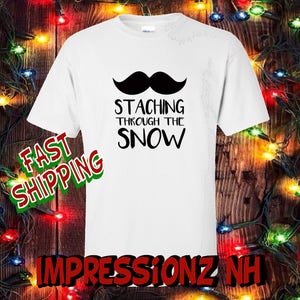 May include: White t-shirt with a black mustache graphic and the text "STACHING THROUGH THE SNOW".