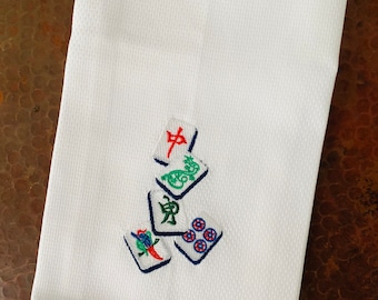 May include: White kitchen towel with embroidered mahjong tiles in red, green, blue, and white.