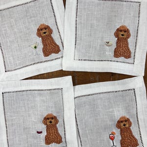 Puede incluir: Juego de cuatro servilletas de cóctel de lino blanco. Cada servilleta presenta un caniche marrón bordado con un cóctel diferente: martini, champán, vino tinto y cóctel con rodaja de naranja. Borde cosido negro.