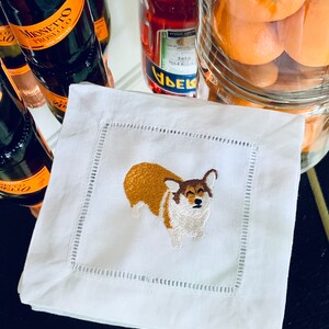 Puede incluir: Servilleta de lino blanco con una imagen bordada de un perro corgi marrón y blanco.