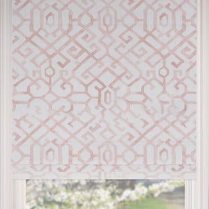 May include: A Roman shade with a geometric pattern in shades of blush pink and white. The fabric is a light color, and the design is a repeating series of interlocking shapes. The shade is partially lowered, revealing a window and a glimpse of the outside.