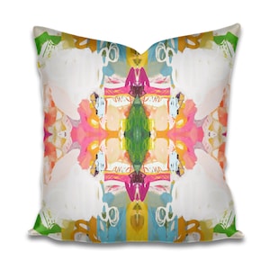 May include: Square throw pillow with an abstract design. The pillow features a symmetrical pattern with white, pink, green, yellow, and blue brushstrokes. The design has a modern, artistic aesthetic, suitable for home decor.