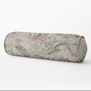 May include: A cylindrical throw pillow with a pink background and a floral pattern featuring birds and branches. The pillow has a subtle textured fabric.