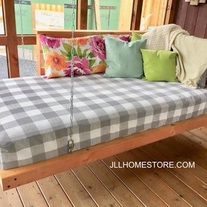 May include: A wooden porch swing with a gray and white checkered cushion. The swing is adorned with colorful throw pillows in shades of pink, orange, green, and blue. A cream-colored blanket is draped over the back. The swing is suspended by metal chains.