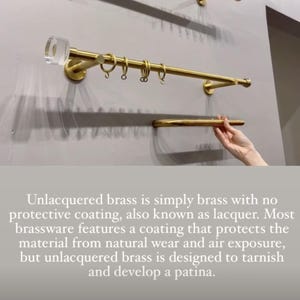 Pu&ograve; includere: Un set di bastoni per tende in ottone dorato contro un muro grigio. L'asta ha estremit&agrave; cilindriche trasparenti e include anelli per appendere le tende. L'immagine mostra anche un ripiano e del testo sull'ottone non verniciato.