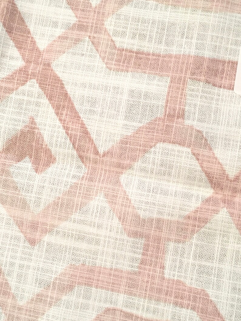 May include: Close-up of a white fabric with a geometric pattern in a soft pink hue. The design features intersecting lines and shapes, creating a textured appearance. The fabric has a slightly sheer quality, suggesting it might be used for clothing or home decor.
