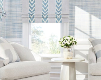 May include: A bright, airy interior scene featuring a window with light blue and white striped Roman shades. Two white armchairs flank a small, round side table holding a vase of white flowers. The walls are a light blue textured pattern.