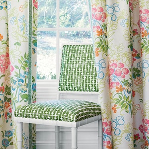 Könnte beinhalten: Ein weißer Stuhl mit einem grün gemusterten Sitz und Rückenlehne. Der Stuhl steht vor einem Fenster mit weißen Vorhängen, die ein Blumenmuster in den Farben Rosa, Orange, Grün und Blau zeigen.