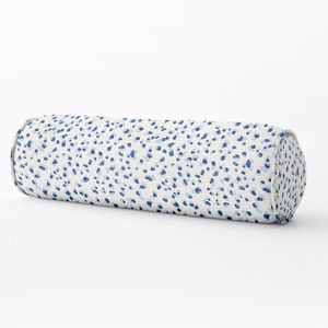 Puede incluir: Una almohada cilíndrica blanca con un patrón de lunares azules y blancos. La almohada está hecha de tela y tiene una forma redondeada.