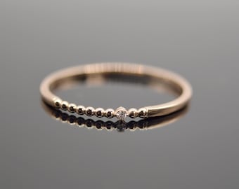 May include: A delicate gold ring with a single small diamond set in the center of a beaded band.