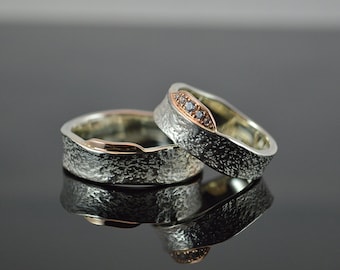 May include: Two silver wedding bands with a textured finish. One band has a thin band of rose gold and two small diamonds.