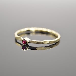 Könnte beinhalten: Ein dünner Goldring mit einem kleinen roten Edelstein in der Mitte.