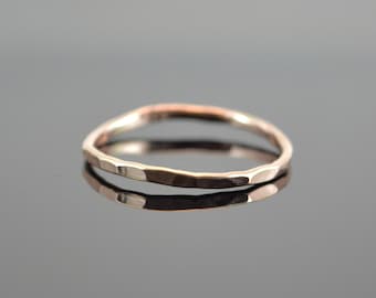 May include: A thin, hammered, rose gold band ring.
