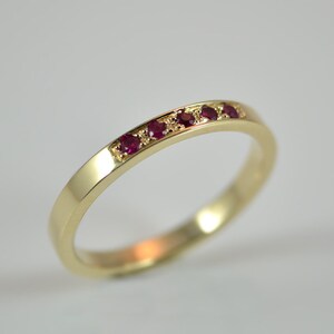Könnte beinhalten: Ein dünner Goldring mit einer Reihe kleiner roter Edelsteine.